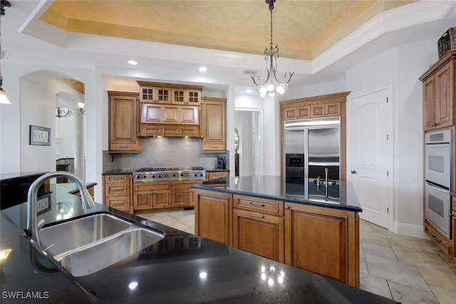 kitchen with stainless steel appliances, decorative light fixtures, a tray ceiling, and a notable chandelier