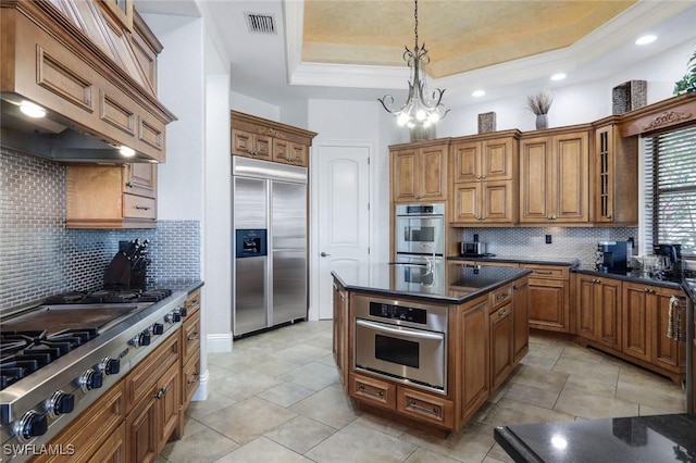 kitchen featuring custom exhaust hood, an inviting chandelier, stainless steel appliances, a tray ceiling, and decorative light fixtures