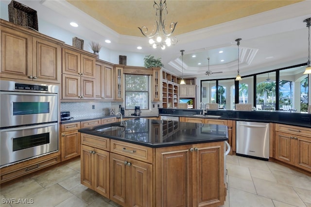 kitchen with kitchen peninsula, hanging light fixtures, stainless steel appliances, a kitchen island with sink, and a tray ceiling