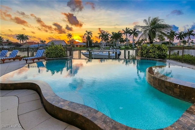 pool at dusk featuring a patio area and an in ground hot tub