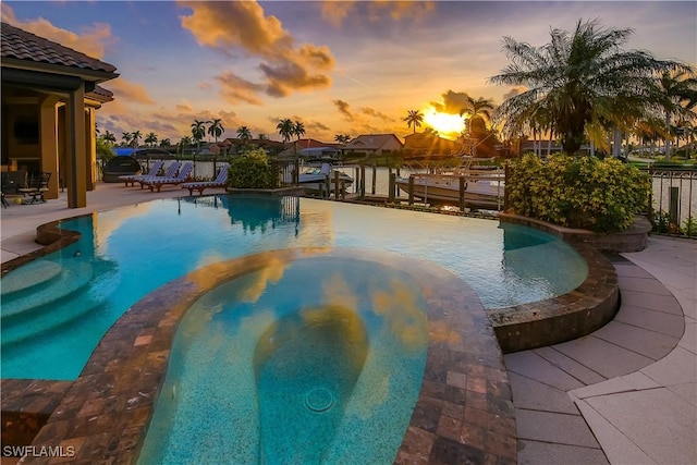 pool at dusk with a patio and an in ground hot tub