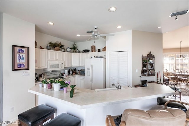 kitchen with a kitchen breakfast bar, white appliances, white cabinetry, and ceiling fan