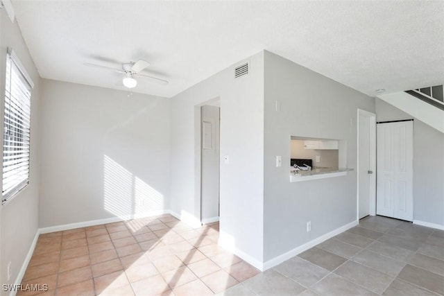 empty room featuring ceiling fan, light tile patterned floors, and a textured ceiling