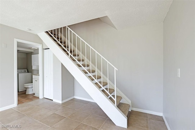 stairs with a textured ceiling, tile patterned flooring, and washer / clothes dryer