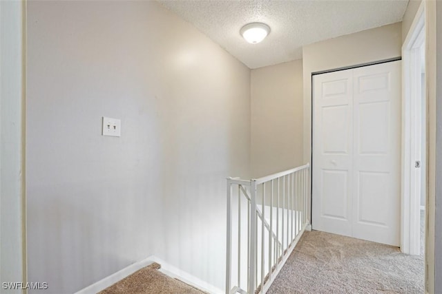 hallway with a textured ceiling and light colored carpet