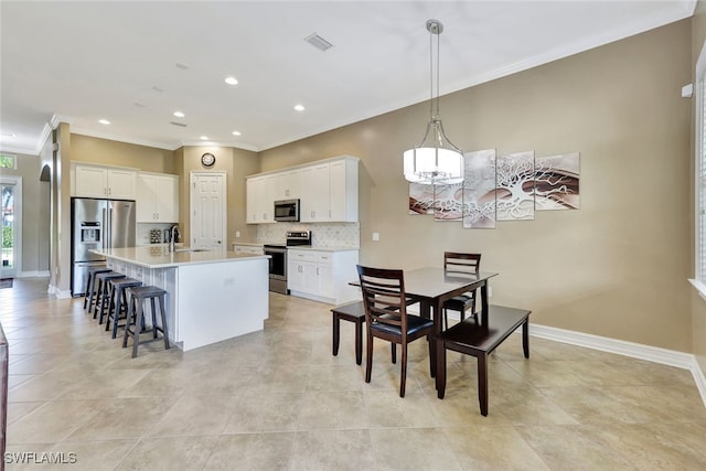 kitchen featuring pendant lighting, white cabinets, stainless steel appliances, decorative backsplash, and a center island with sink