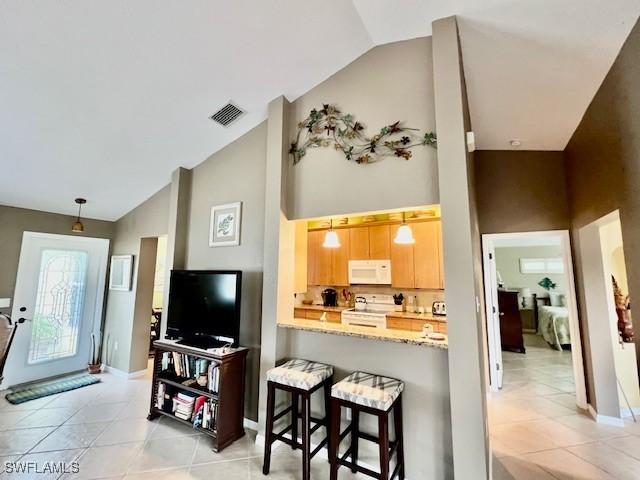 kitchen featuring white appliances, kitchen peninsula, light stone counters, vaulted ceiling, and a kitchen bar