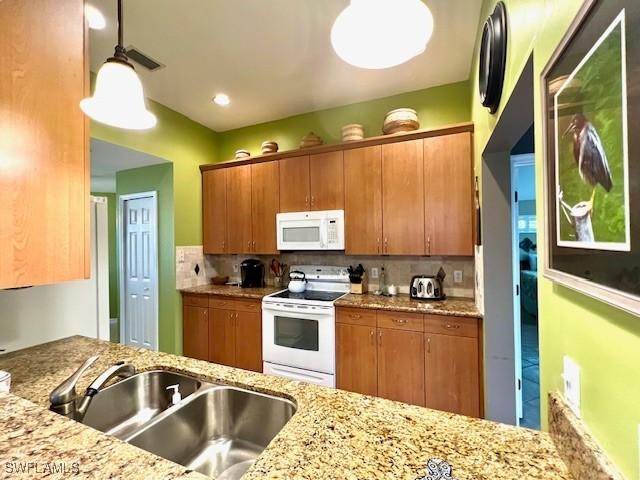 kitchen featuring white appliances, hanging light fixtures, light stone counters, sink, and tasteful backsplash