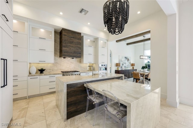 kitchen featuring beam ceiling, an island with sink, white cabinetry, and a kitchen bar