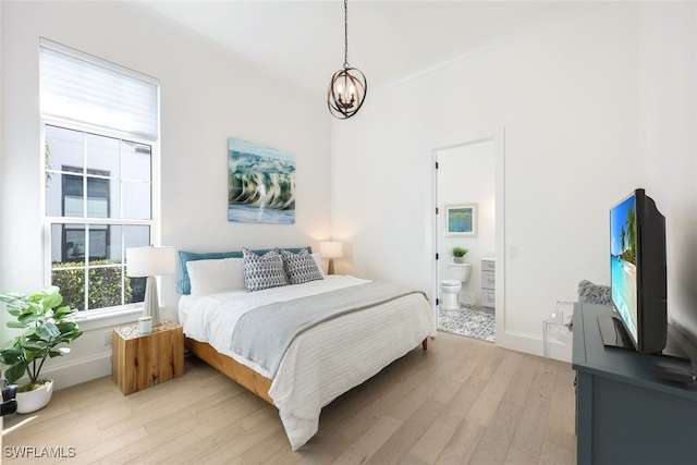 bedroom featuring a notable chandelier, connected bathroom, and light hardwood / wood-style flooring