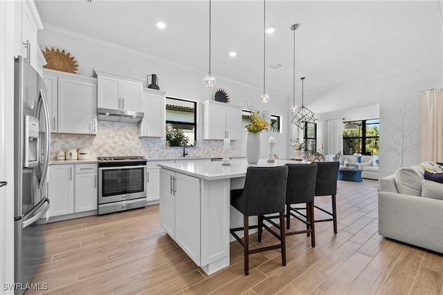 kitchen featuring stainless steel appliances, a breakfast bar, a kitchen island, white cabinetry, and decorative light fixtures