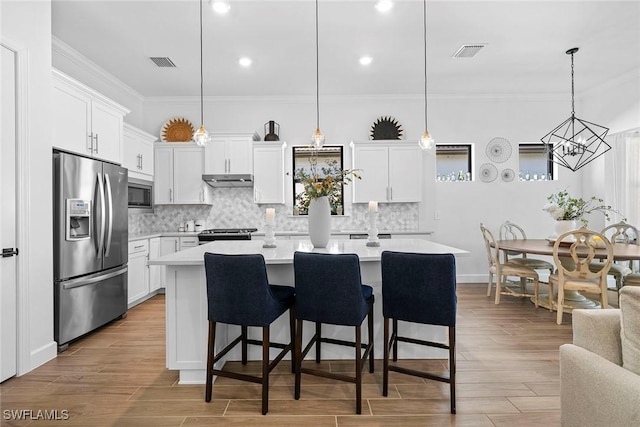 kitchen with white cabinets, stainless steel appliances, a kitchen island, and hanging light fixtures