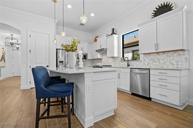 kitchen featuring white cabinets, a center island, pendant lighting, crown molding, and appliances with stainless steel finishes