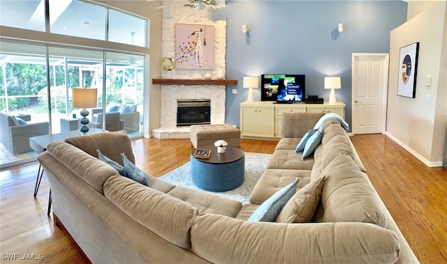 living room with a stone fireplace, a towering ceiling, and light hardwood / wood-style flooring