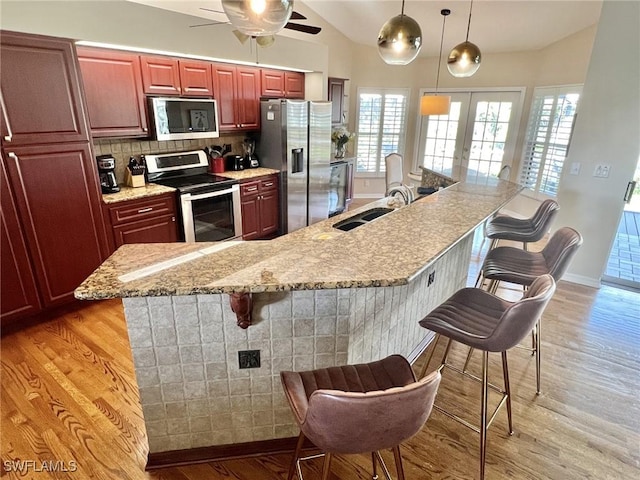 kitchen with sink, stainless steel appliances, a kitchen breakfast bar, decorative backsplash, and light wood-type flooring