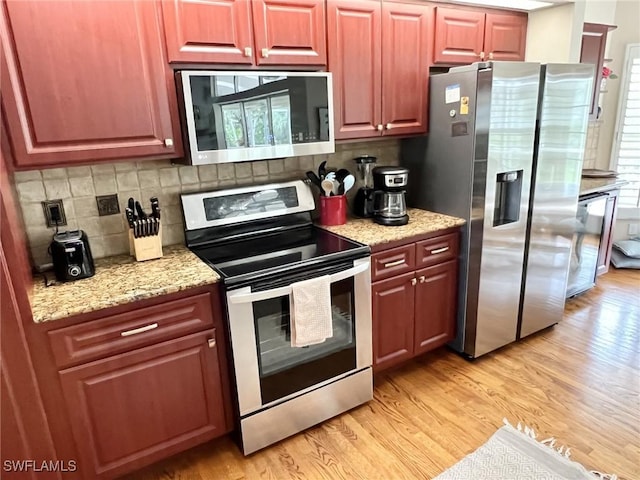 kitchen with light stone counters, appliances with stainless steel finishes, light hardwood / wood-style floors, and decorative backsplash