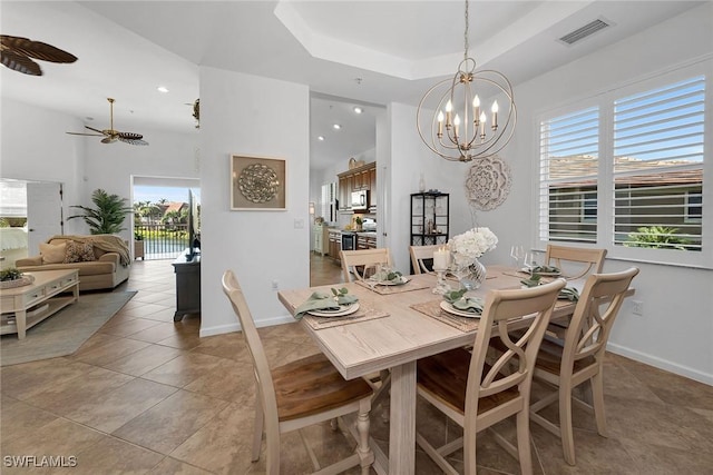 tiled dining area with ceiling fan with notable chandelier and a tray ceiling