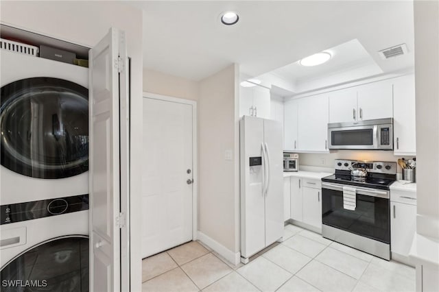 kitchen with a raised ceiling, stacked washer and clothes dryer, stainless steel appliances, and white cabinetry