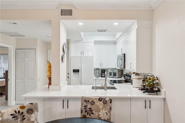 kitchen with white cabinets, stove, white fridge with ice dispenser, and kitchen peninsula