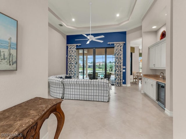 living room featuring ceiling fan, crown molding, a raised ceiling, wet bar, and wine cooler