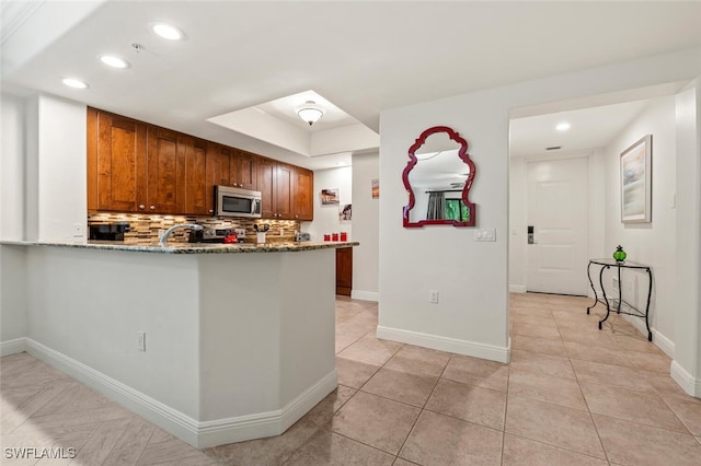 kitchen featuring sink, a tray ceiling, kitchen peninsula, light stone countertops, and decorative backsplash