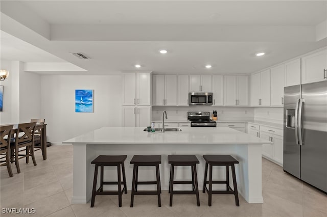 kitchen with a breakfast bar, sink, white cabinets, stainless steel appliances, and a center island with sink