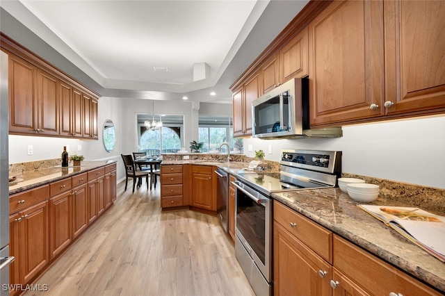 kitchen with stainless steel appliances, sink, light hardwood / wood-style floors, light stone countertops, and a notable chandelier