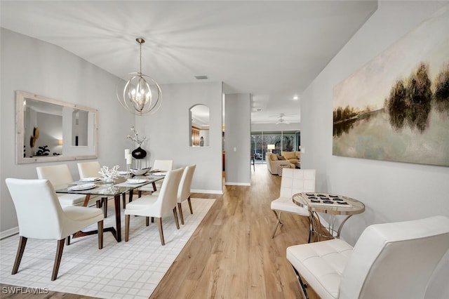 dining space with ceiling fan with notable chandelier and light hardwood / wood-style flooring