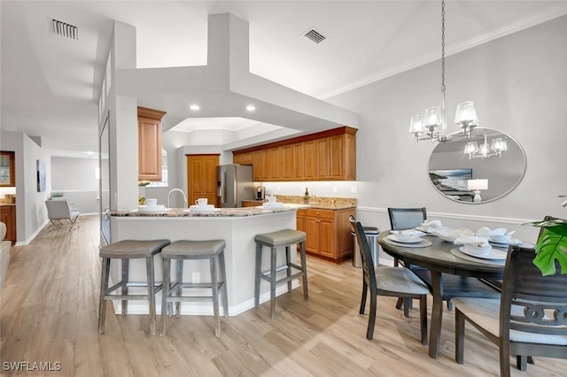 kitchen featuring decorative light fixtures, light stone counters, stainless steel fridge, a chandelier, and crown molding