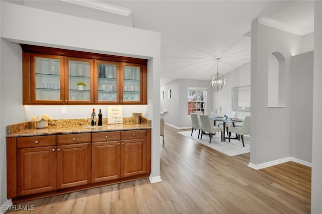 bar featuring lofted ceiling, light hardwood / wood-style flooring, light stone countertops, a chandelier, and pendant lighting