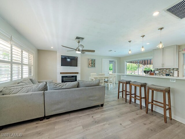 living room featuring ceiling fan, a large fireplace, and light wood-type flooring