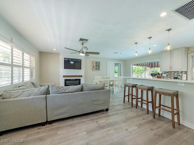 living room featuring plenty of natural light, a large fireplace, ceiling fan, and light wood-type flooring