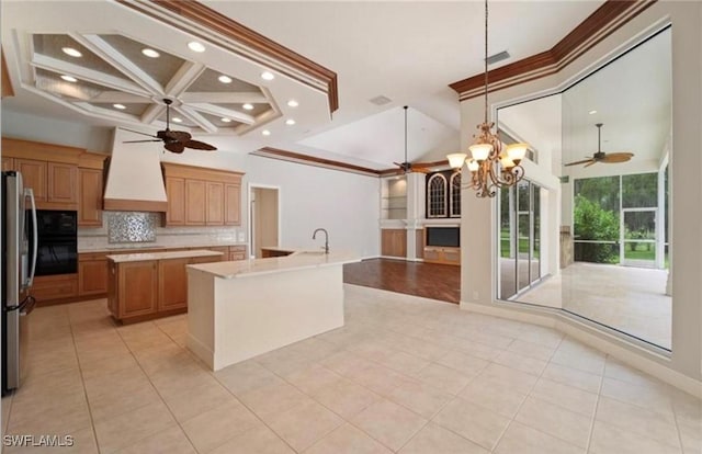 kitchen featuring premium range hood, stainless steel fridge, a kitchen island with sink, ceiling fan with notable chandelier, and backsplash