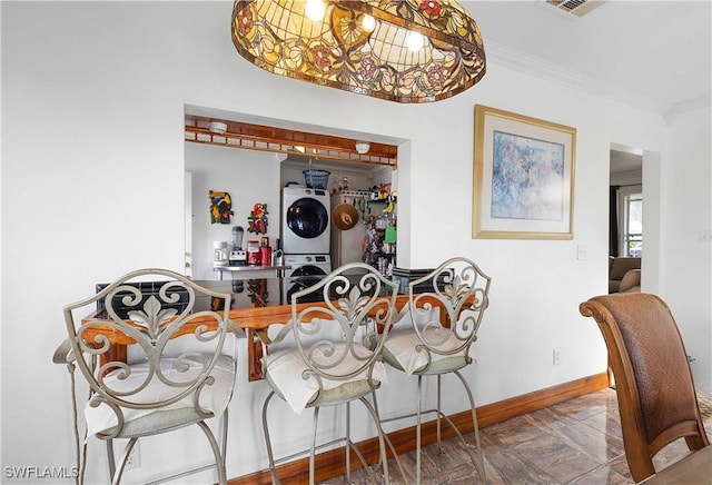 dining space featuring ornamental molding, parquet flooring, and stacked washer and clothes dryer