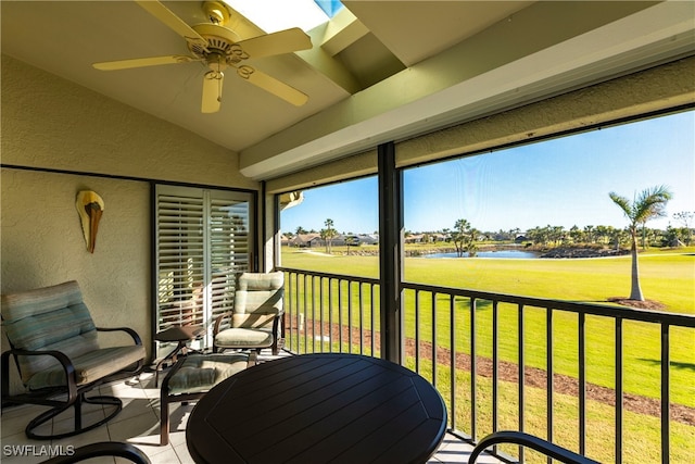 sunroom / solarium featuring ceiling fan, vaulted ceiling with skylight, and a water view