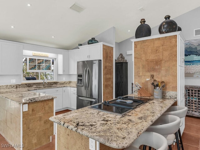 kitchen with stainless steel refrigerator with ice dispenser, white cabinets, a breakfast bar area, and vaulted ceiling