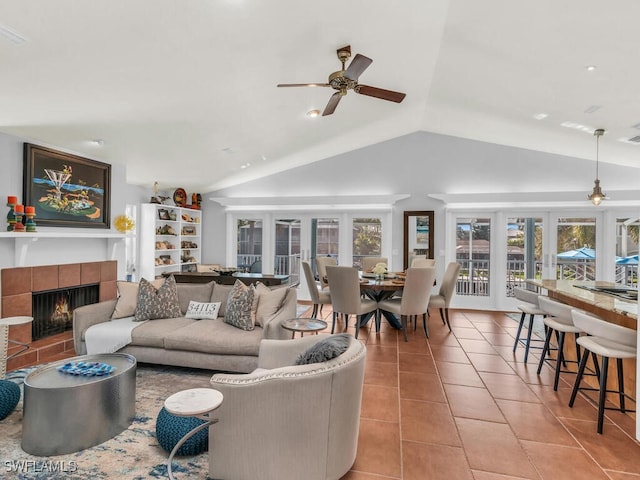 living room with ceiling fan, vaulted ceiling, light tile patterned flooring, a tiled fireplace, and french doors