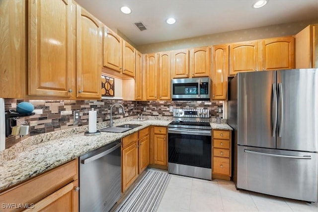 kitchen with appliances with stainless steel finishes, light stone countertops, light tile patterned floors, sink, and backsplash