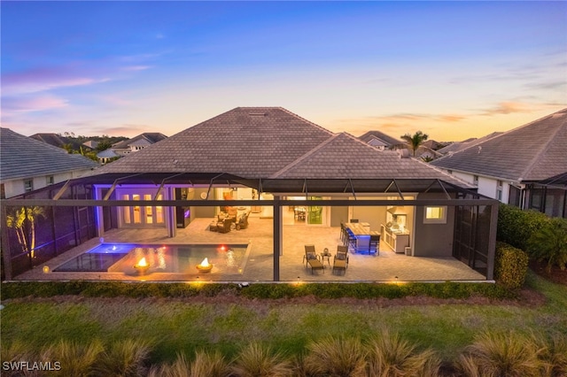 back house at dusk featuring a patio and glass enclosure