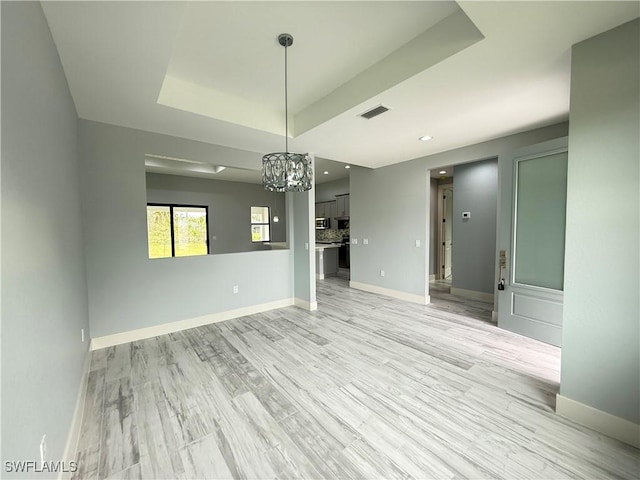 interior space featuring light hardwood / wood-style floors, a raised ceiling, and a notable chandelier