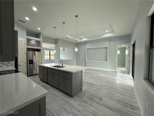 kitchen featuring pendant lighting, gray cabinetry, sink, stainless steel fridge with ice dispenser, and a center island with sink