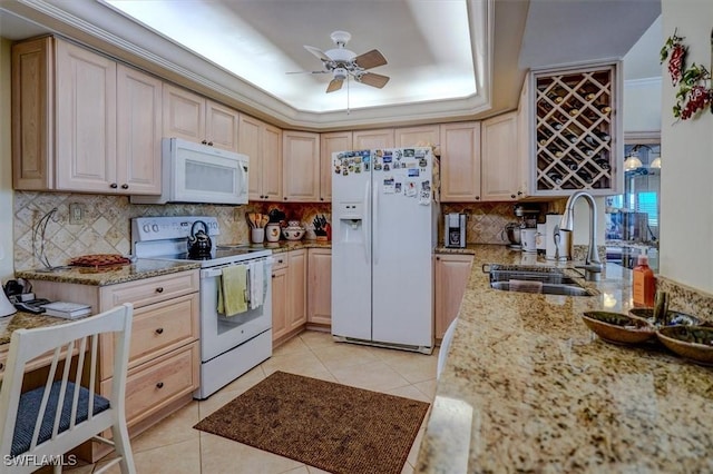 kitchen with light stone counters, white appliances, a raised ceiling, and sink