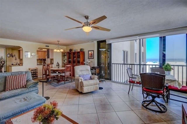 living room featuring light tile patterned floors, floor to ceiling windows, a water view, a textured ceiling, and ceiling fan with notable chandelier