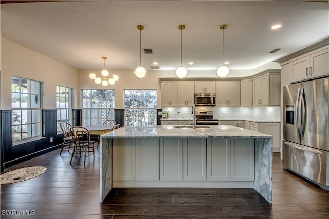 kitchen featuring light stone countertops, appliances with stainless steel finishes, hanging light fixtures, an island with sink, and dark hardwood / wood-style floors