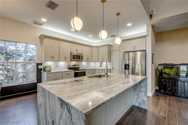 kitchen featuring decorative light fixtures, stainless steel appliances, sink, backsplash, and light stone counters