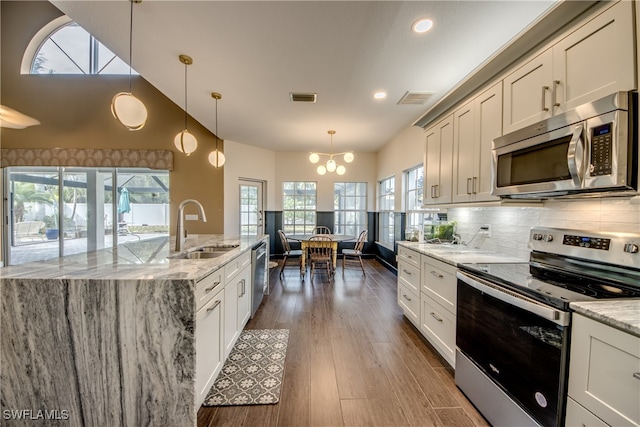 kitchen with light stone countertops, tasteful backsplash, sink, decorative light fixtures, and stainless steel appliances