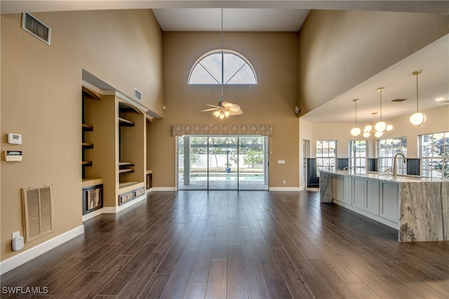 unfurnished living room featuring ceiling fan with notable chandelier, dark wood-type flooring, built in shelves, and a high ceiling