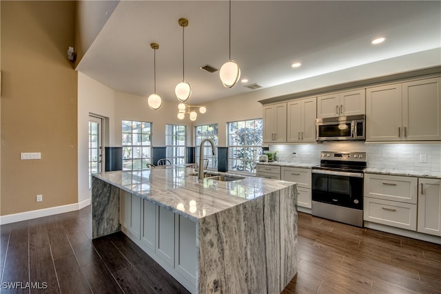 kitchen with light stone countertops, sink, appliances with stainless steel finishes, and a kitchen island with sink