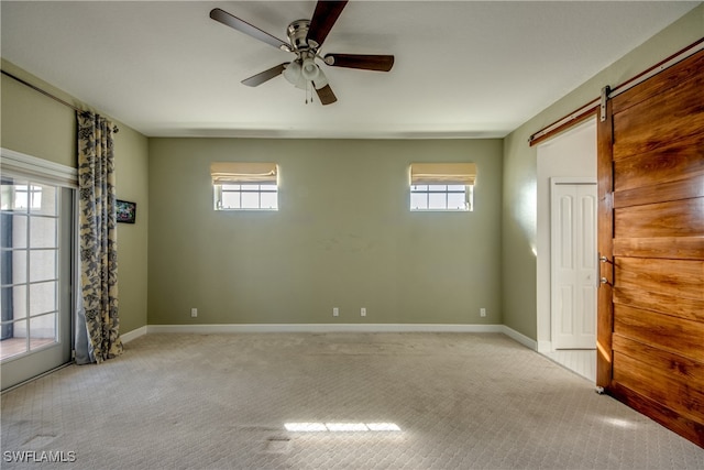 carpeted spare room with plenty of natural light, ceiling fan, and a barn door