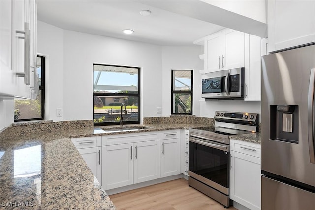 kitchen featuring stainless steel appliances, sink, white cabinets, light stone counters, and light wood-type flooring